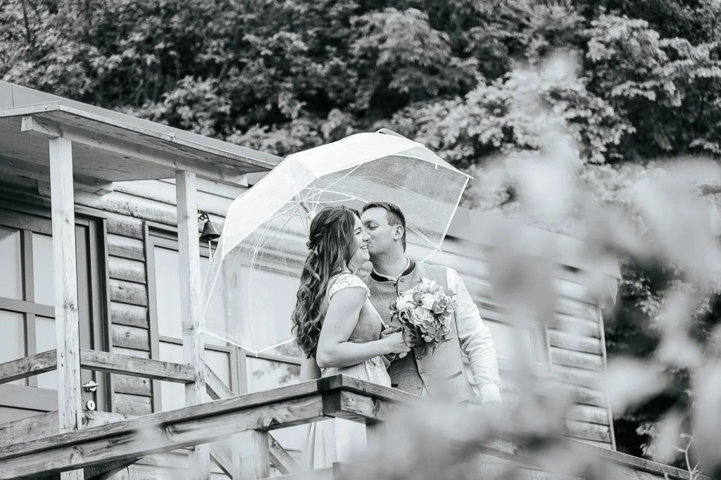 Natürliche Hochzeitsfotos mit Regenschirm Brautpaar küsst sich unter Regenhimmel