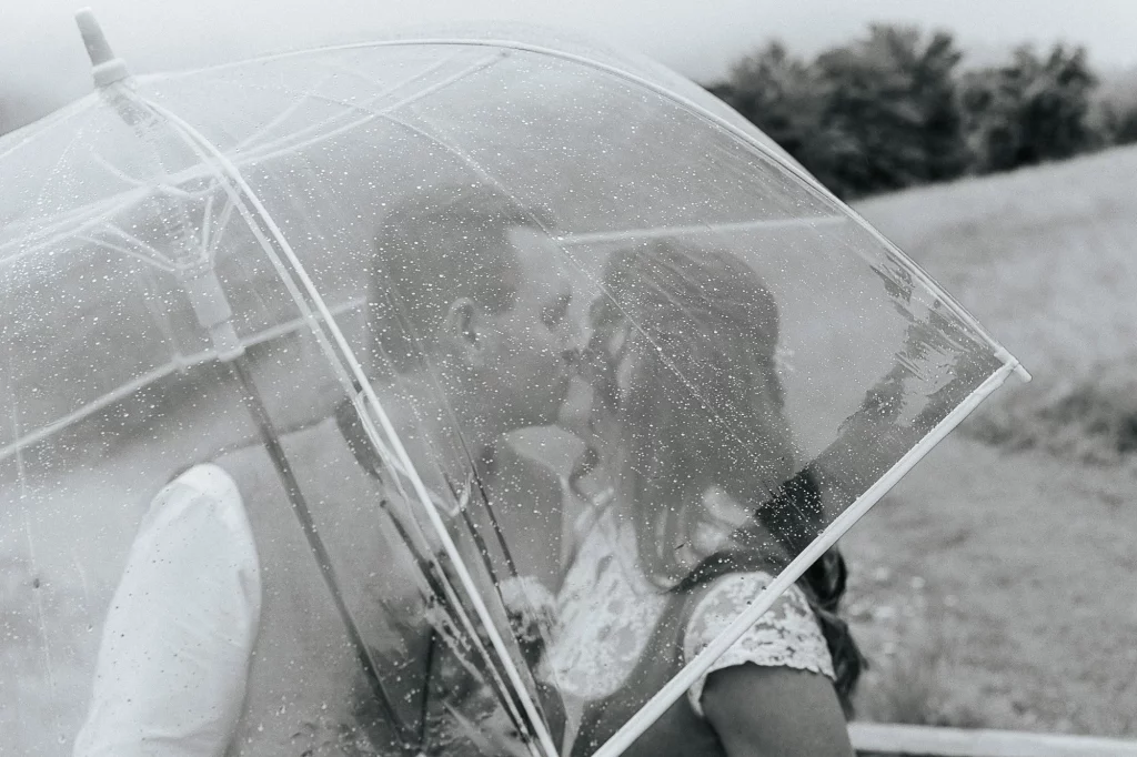 Hochzeitsfotos im Regen Brautpaar küsst sich unter Regenschirm